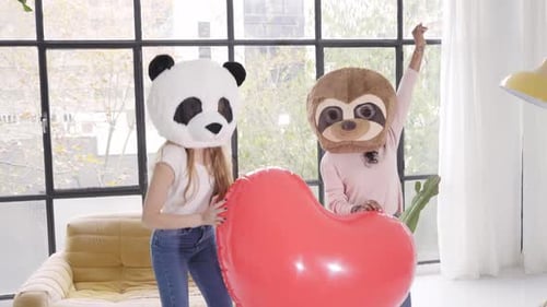 Mujeres divertidas con máscara de animal, oso panda con un gran corazón bailando en casa, felices emociones positivas