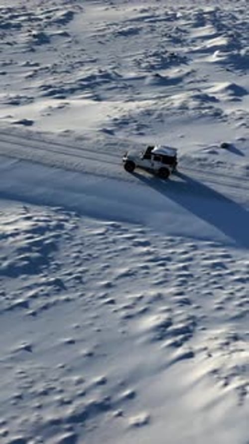 Vertical aerial view of a white off road vehicle driving along a snow covered track across the