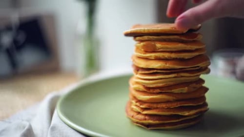 Man takes one delicious pancake from stacked american pancakes on green plate