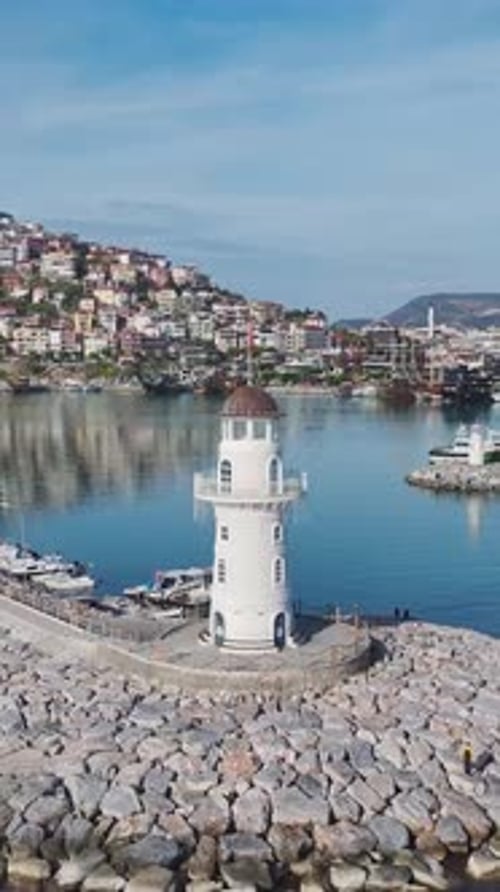 Vertical Video of a Tall White Lighthouse in the Port Captured From Above Overlooking the Ocean and