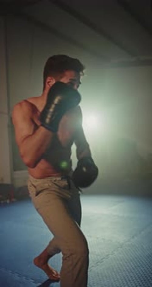 Boxer Training with Heavy Bag in Dark Gym