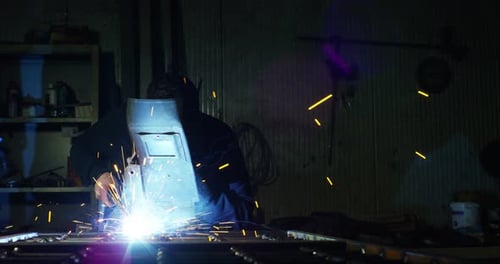 Welder Works on Metal in Dark Workshop
