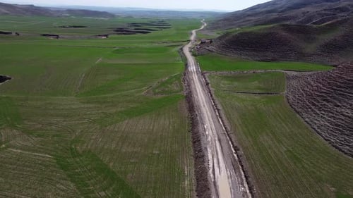 Aerial view of muddy and dusty road between green fields 4K