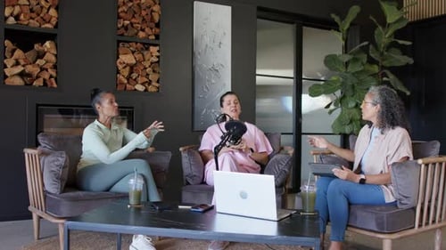 Leaning left host gesturing, co-hosts filming podcast, center in pink speaking into mic in studio