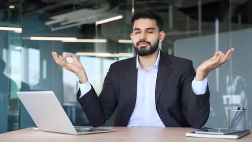 Bearded Man Meditating at Office Desk with Laptop