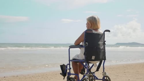 Elderly Asian woman sitting in wheelchair Gazing at the sea and the people who are happy to relax