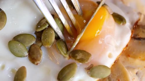 A Deliciously Cooked Egg Accompanied By Crunchy Pumpkin Seeds and a Fork on a Plate