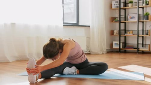 Woman Stretching Legs on Yoga Mat in Bright Room