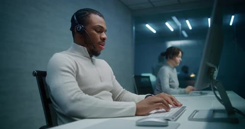 Call Center Office at Night African American Technical Support Specialist in Headset Works on PC