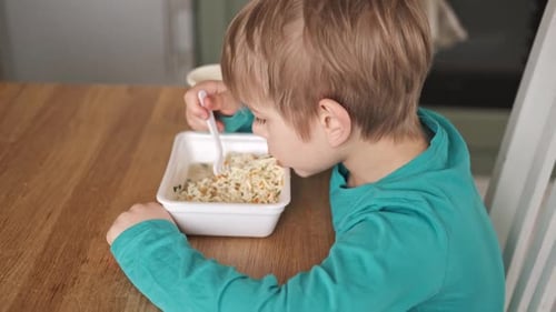 Child Eats Takeout Noodles at Wooden Table