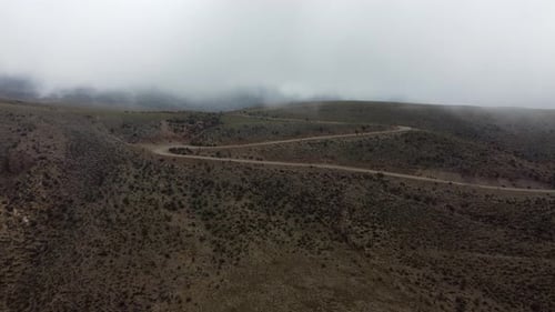 Large looping switchback leads gravel road off foggy rolling plateau