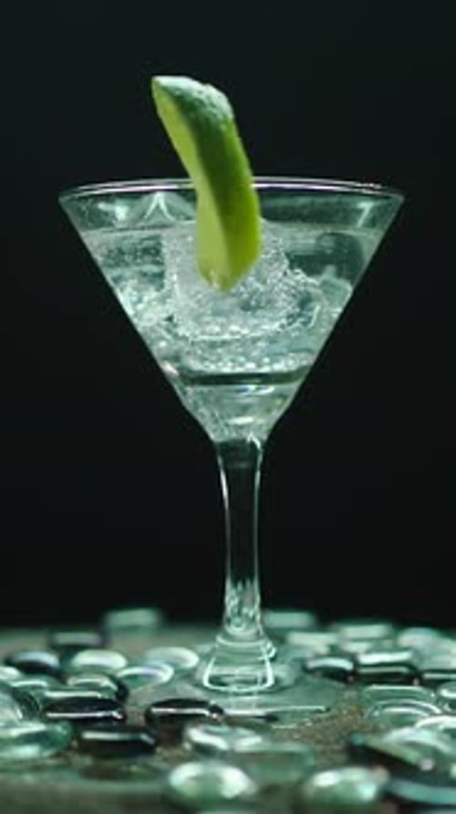 Martiniglas mit rotierender Limette auf schwarzem Hintergrund