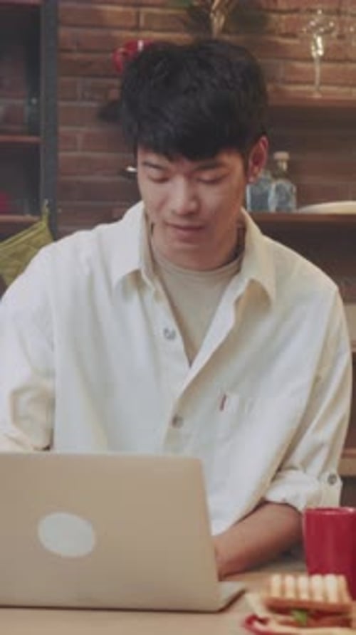 Student Working on Computer Asian Student Concentrating on Coursework While Relaxing in Cozy Cafe
