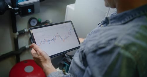 Worker Monitoring Exchange Market Charts Using Digital Tablet in Workshop