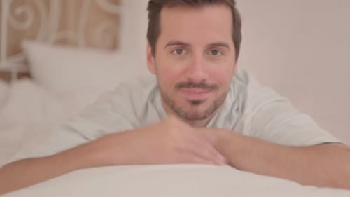 Jeune homme faisant les pouces levés en position couchée sur le ventre dans son lit