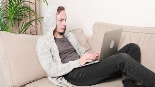 Ein junger Mann arbeitet zu Hause auf der Couch und trinkt heißen Kaffee in einer weißen Tasse