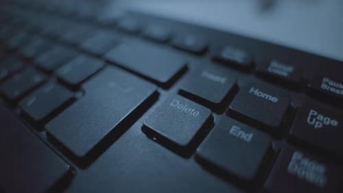 Nahaufnahme auf der Computertastatur, während die Hand die Löschtastatur im dunklen Raum drückt. Büro oder Zuhause. Geheim