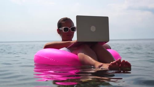 Woman Freelancer Works on Laptop Swimming in Sea on Pink Inflatable Ring Happy Tourist in Sunglasses