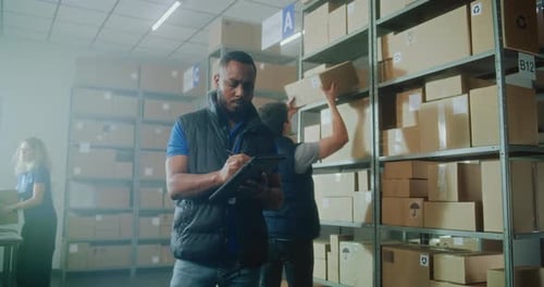 African American Male Logistics Specialist Uses Tablet Computer and Stylus Checks Inventory