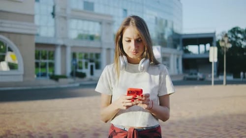 Beautiful Young Woman Uses a Smartphone on the Street Portrait of a Beautiful Girl with Headphones