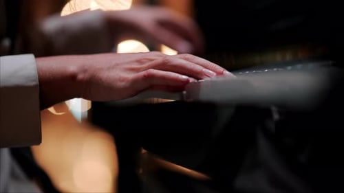Close up of a woman's hands playing the piano with blurry lights on the background