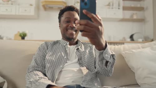 Young Adult Video Calling on Smartphone on Sofa
