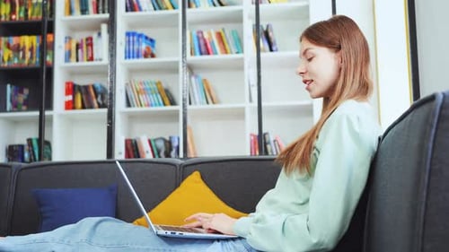 Young Female Student Video Chatting Via Laptop in Library