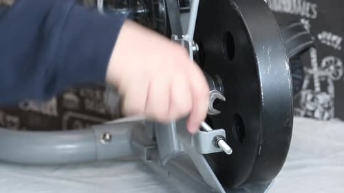 Um homem remove um rolo de pressão para acionar uma correia em uma bicicleta ergométrica. Solte as porcas do tensor
.