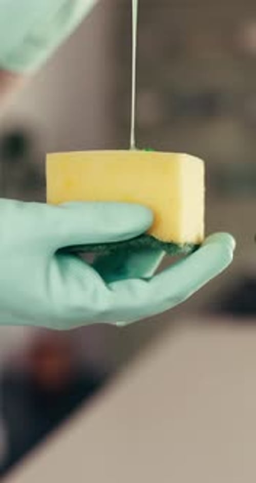 Pouring green cleaning liquid onto a yellow sponge