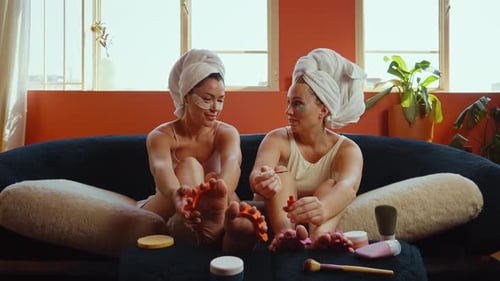 Women painting toenails and relaxing on sofa