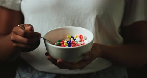 Hands, bowl and pills for abuse in studio with eating for mind altering drugs by black background