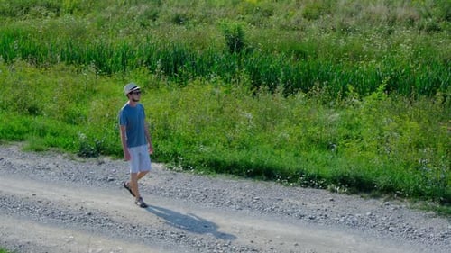 Man Walking Along a Rural Dirt Road Surrounded By Fields
