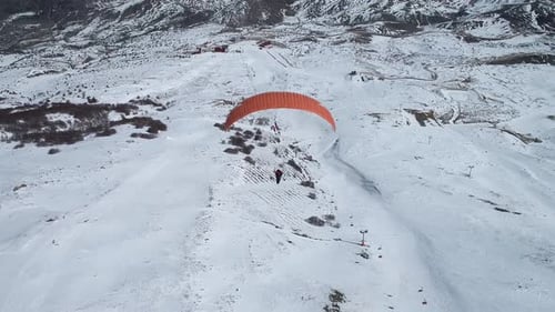 Luftaufnahme eines Mannes beim Gleitschirmfliegen auf einem Berg im Winter
