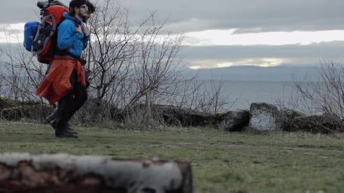 Two males backpackers walk on hiking path by coast. Ocean horizon in background