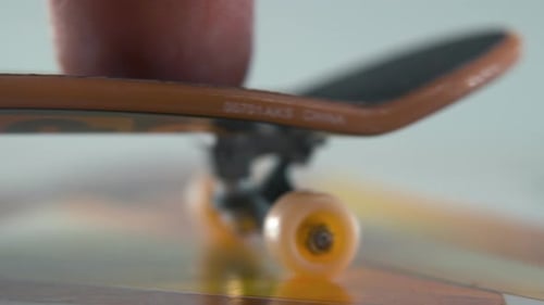 A hyper close-up detailed shot of a mini skateboard, tiny white wheels, riding fingerboard from left