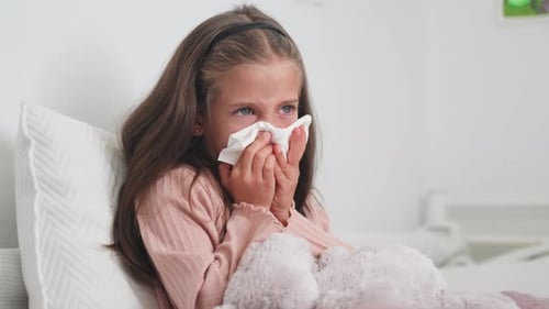 Sick Child Wipes Nose in Bed with Tissue