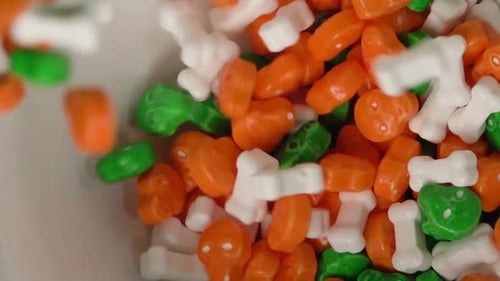 Orange and green skulls and bones shaped candy falling on a plate.