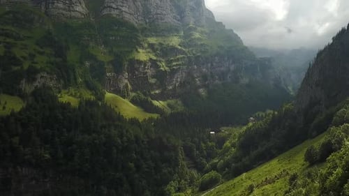 Forward flight over beautiful green forest in a cloudy day. Surrounded by mountains and rocks