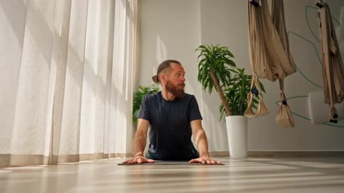 adult man with beard doing back stretch on exercise mat yoga active lifestyle trainer in own studio