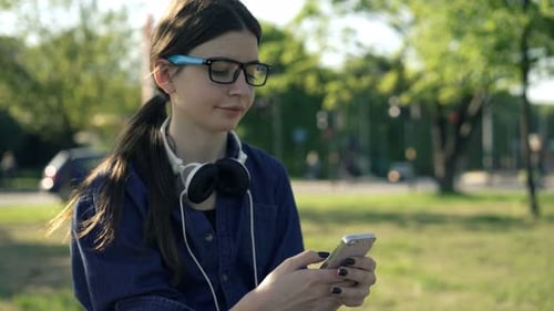 Teenage Girl Surfing Internet On Smartphone Sitting In City Park