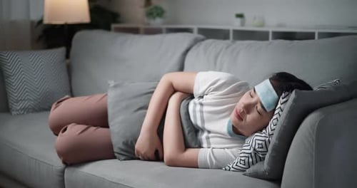 Jeune femme ayant mal au ventre et à la tête sur le canapé à la maison.
