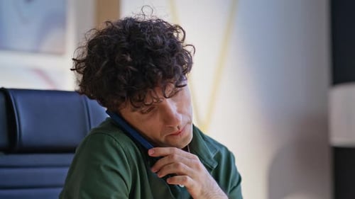 Young Adult Talks on Phone While Working on Laptop