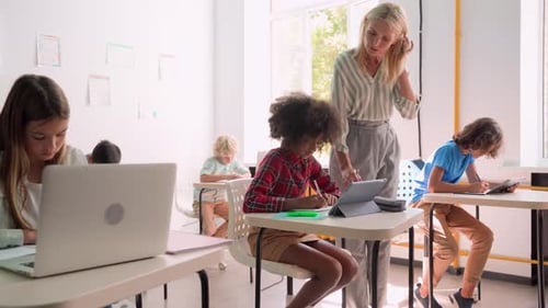 Teacher Helping Students in Classroom with Tablets