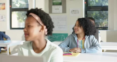 African American teen girls turning toward teacher after prompt in classroom smiling with notebook