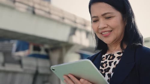Smiling Woman Standing and Using Tablet Outdoors Working Remotely Old Lady in Street Watching Video