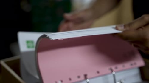 Close-up of hands sorting and organizing documents in a pink binder folder, depicting office work, p