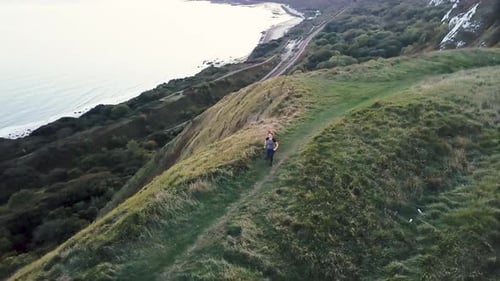 View from drone on young adult female running on cliff by sea
