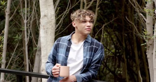 Young man enjoying coffee outdoors in forest, wearing casual plaid shirt