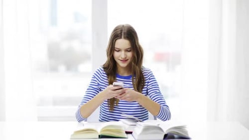 Smiling Girl Using Smartphone with Books on Desk