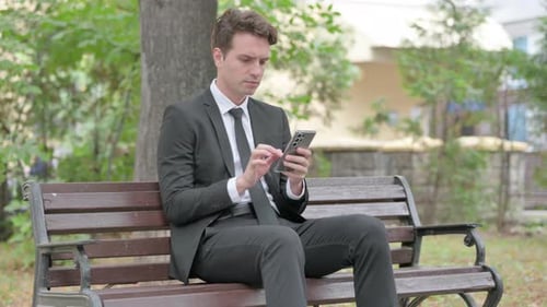 Man in Suit Using Phone on Park Bench